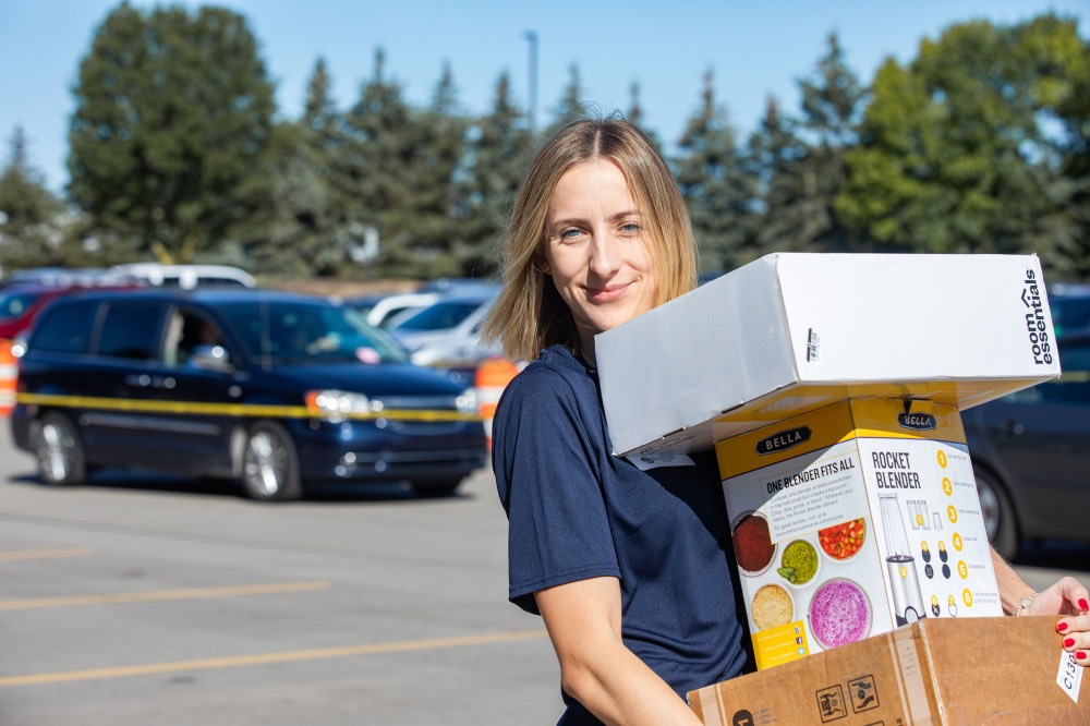 GVSU Alumna smiles as she carries a stack of 3 boxes